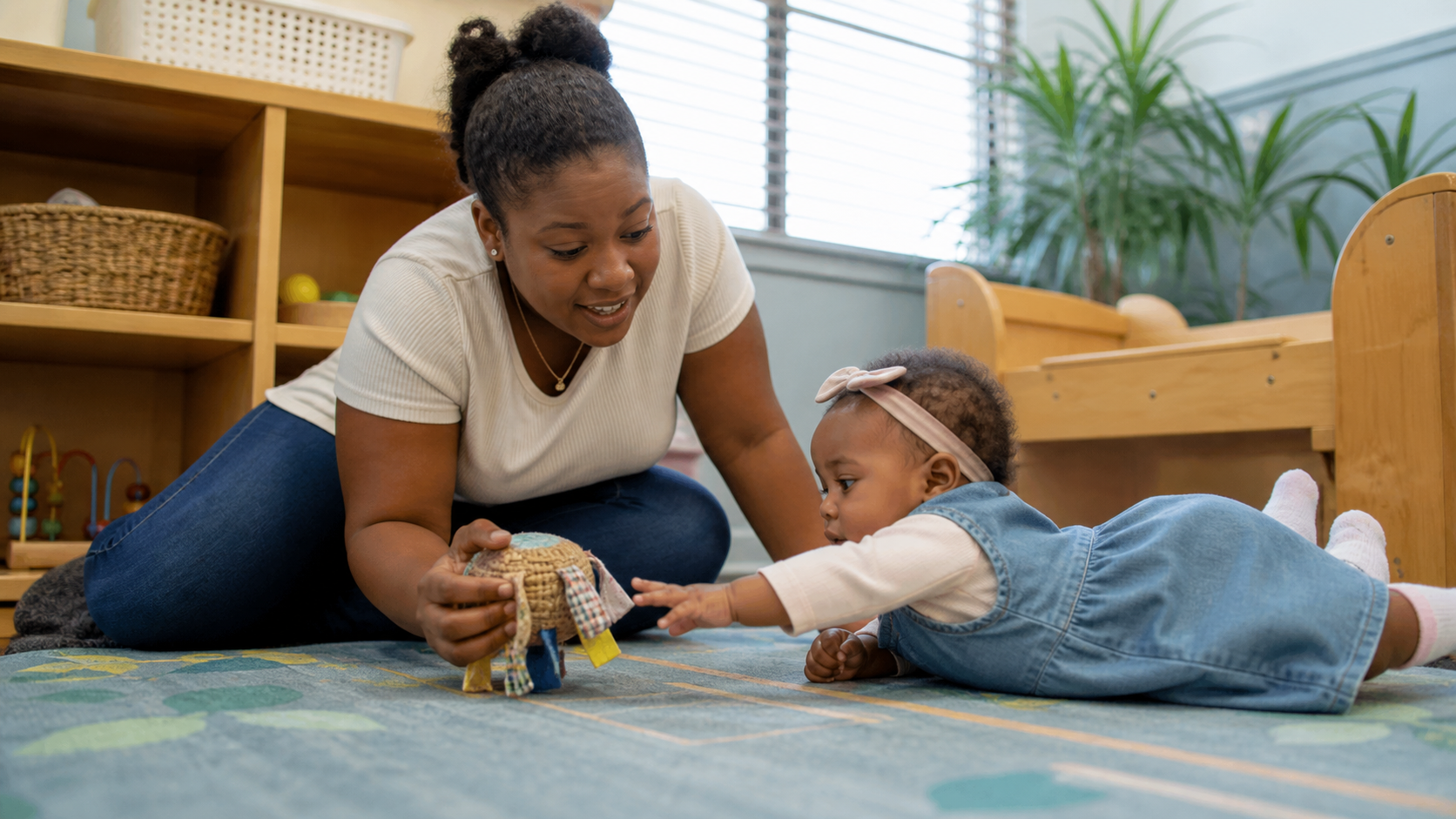 Caregiver engaging an infant with a soft toy on a classroom rug